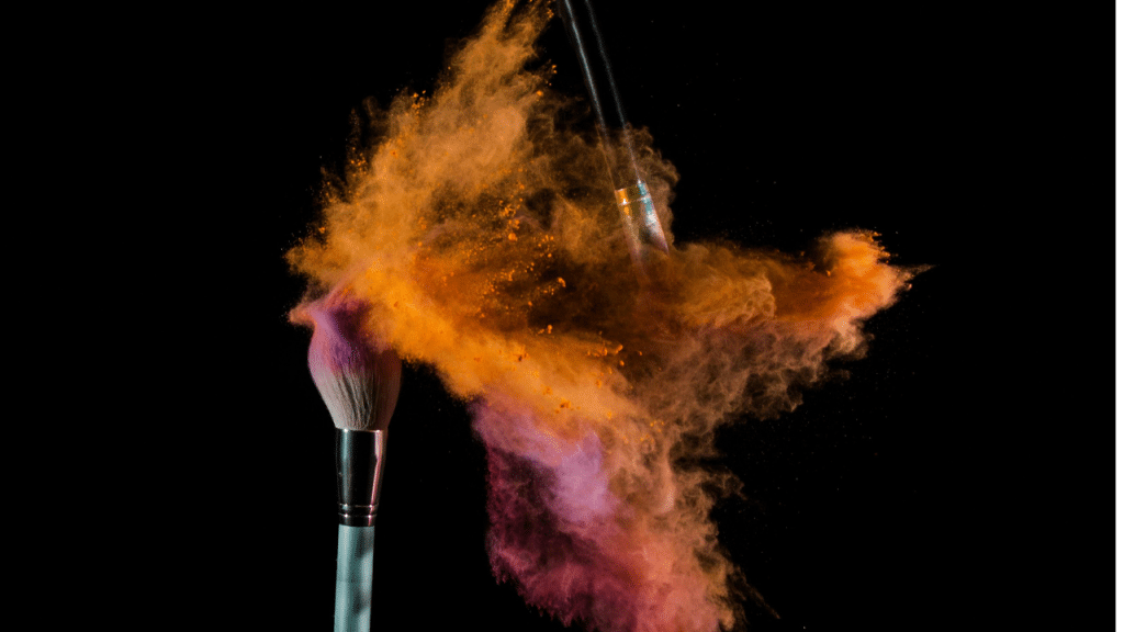 Deux pinceaux de maquillage qui s'entrechoquent, dispersant de la poudre de couleur autour
