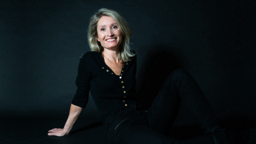 Stephanie Romeo, seated and smiling, wearing a black outfit.