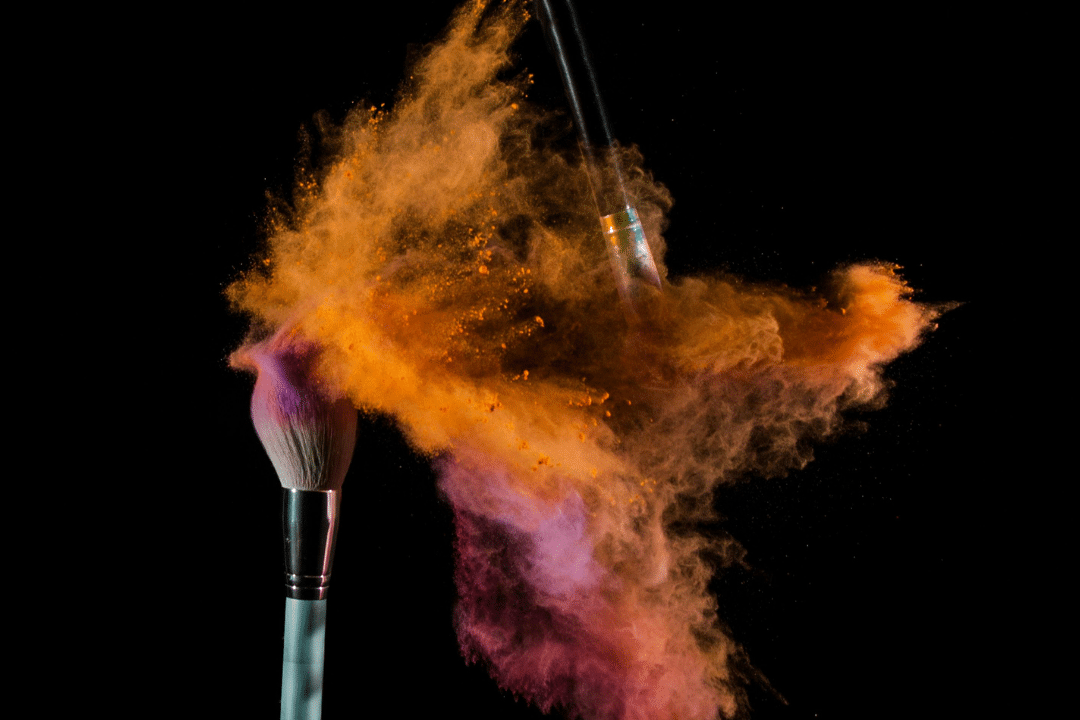 Deux pinceaux de maquillage qui s'entrechoquent, dispersant de la poudre de couleur autour