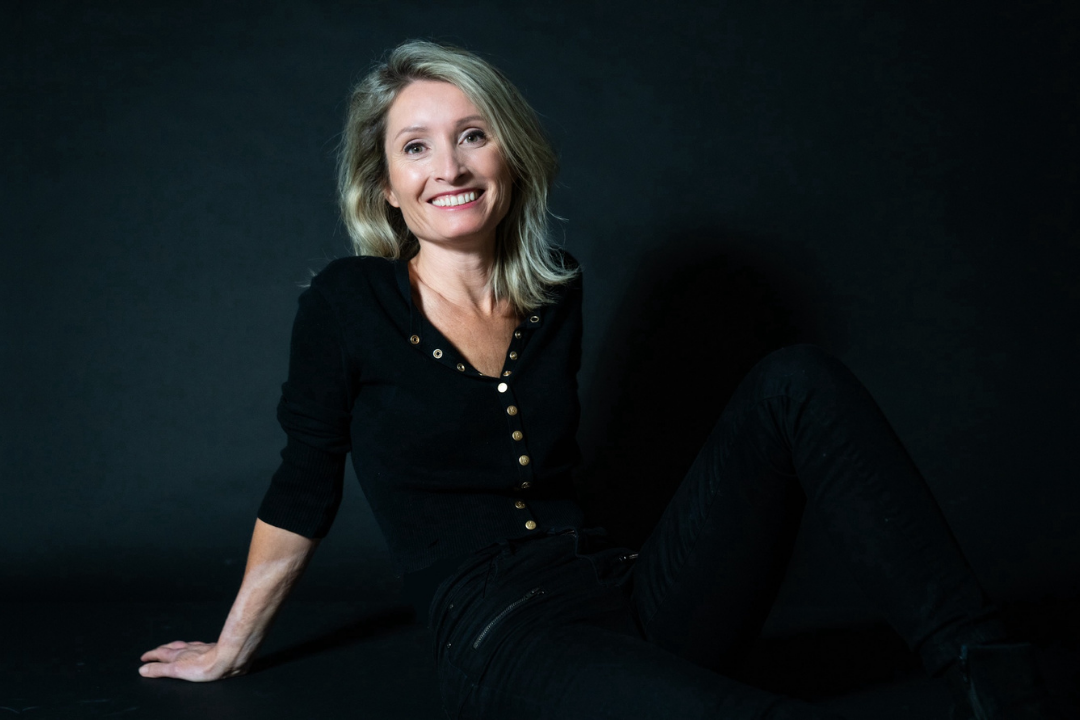 Stephanie Romeo, seated and smiling, wearing a black outfit.